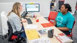 University College employee meeting with smiling student at office desk.